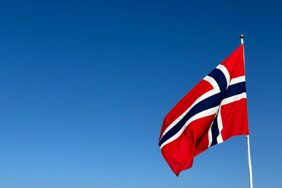 Norwegian flag waving in clear blue sky, symbolizing patriotism and national pride.