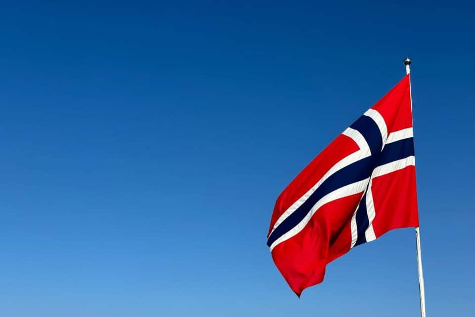 Norwegian flag waving in clear blue sky, symbolizing patriotism and national pride.