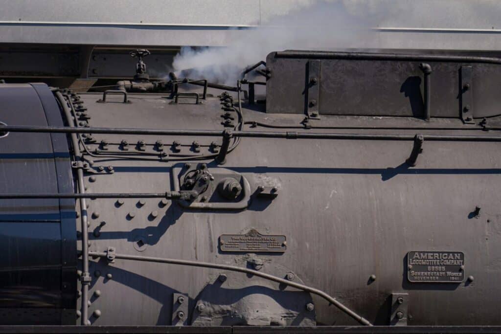 Detailed view of an American steam locomotive engine emitting steam, showcasing industrial design.