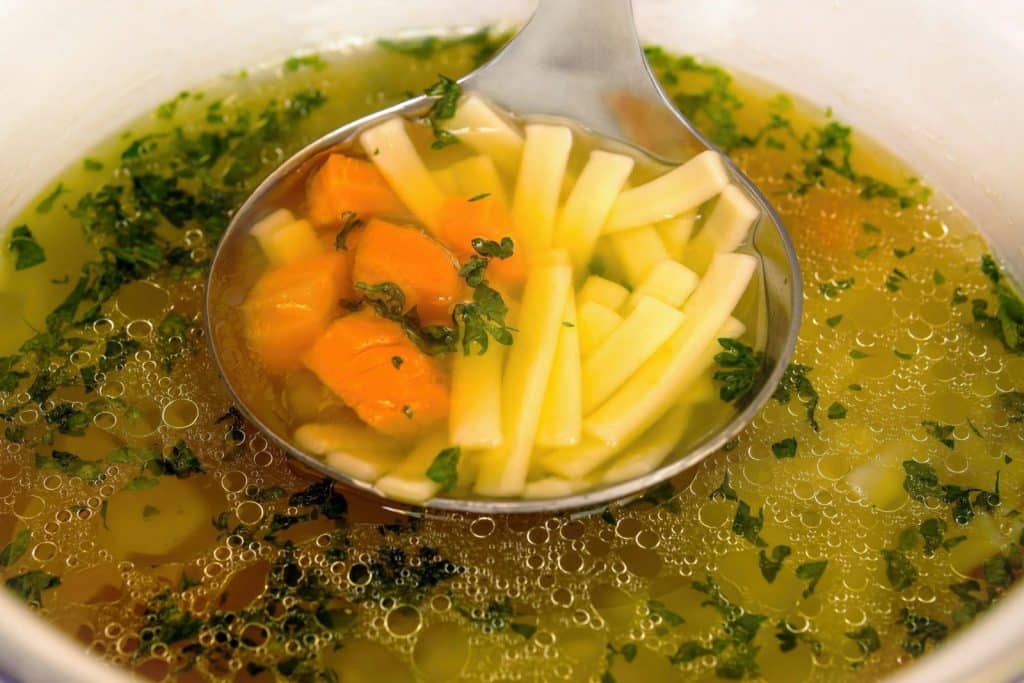 A steaming ladle of chicken broth with carrots and herbs, perfect for a cozy meal.