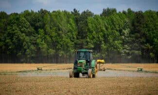 Tractor spraying fields with pesticides on a countryside farm in summer with a forest backdrop.