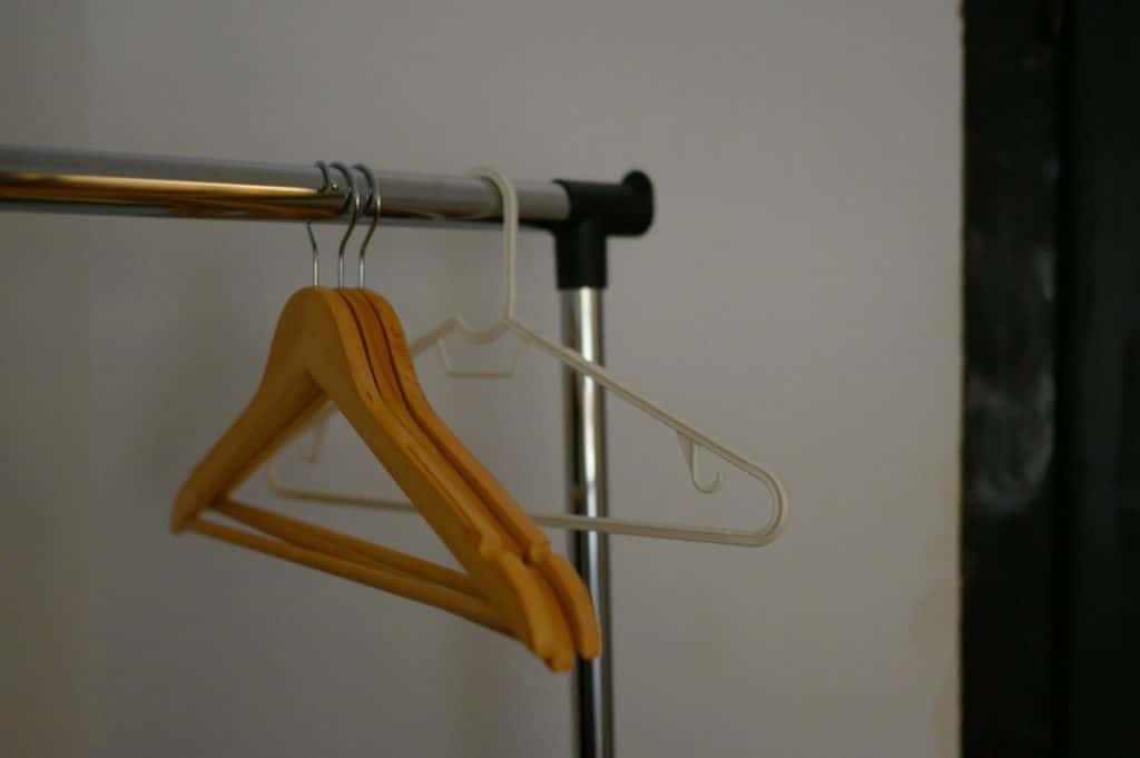 Wooden and plastic hangers on a clothing rack in a minimalist indoor setting.
