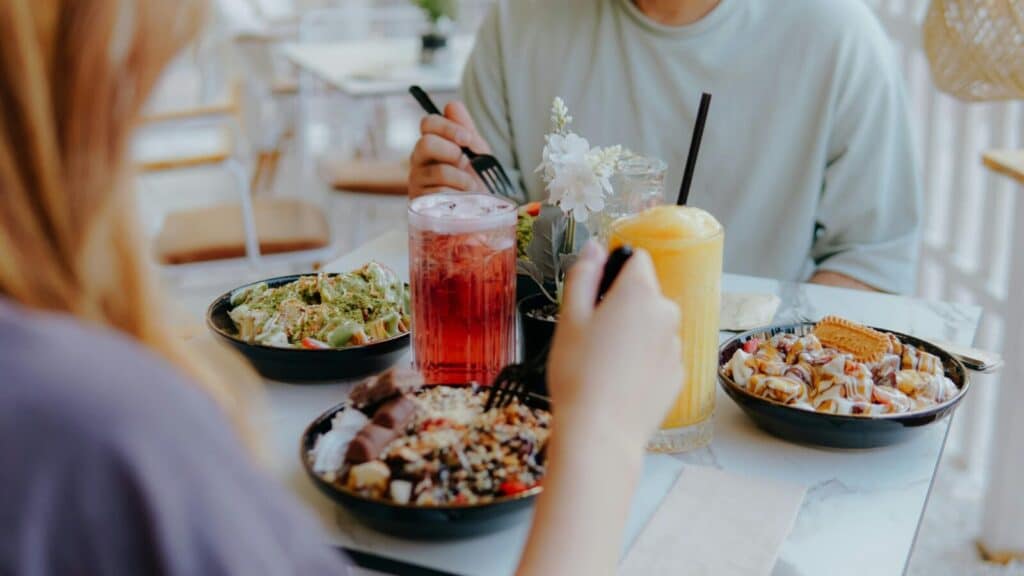 Two people enjoying a casual meal with various lunch bowls and refreshing drinks at a light-filled café.