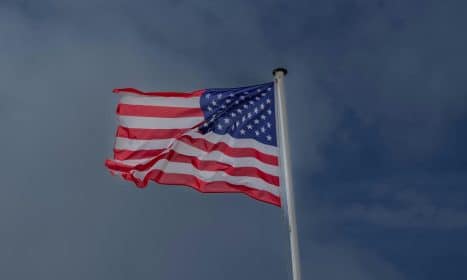 A vibrant American flag waving in the wind against a clear sky at Omaha Beach, France.