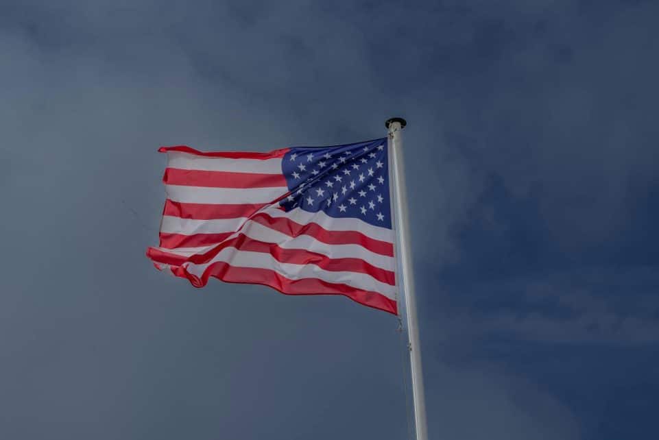 A vibrant American flag waving in the wind against a clear sky at Omaha Beach, France.