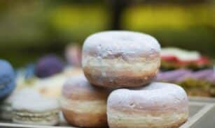 Close-up of three powdered donuts stacked on a wooden tray outdoors.