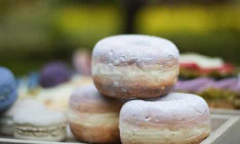 Close-up of three powdered donuts stacked on a wooden tray outdoors.