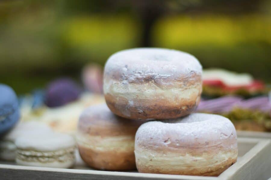 Close-up of three powdered donuts stacked on a wooden tray outdoors.