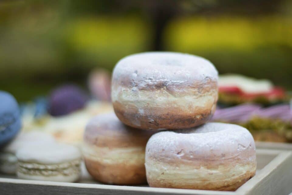 Close-up of three powdered donuts stacked on a wooden tray outdoors.