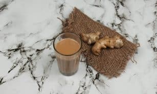 A glass of traditional Indian masala chai served with fresh ginger on a marble countertop.