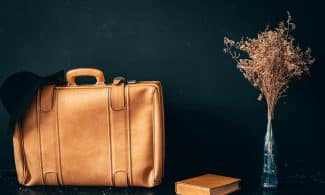 A vintage leather suitcase paired with dried flowers in a vase and a book on a dark background.