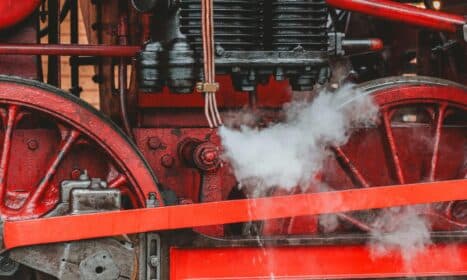 Detailed view of a red vintage steam locomotive engine showcasing gears and steam.