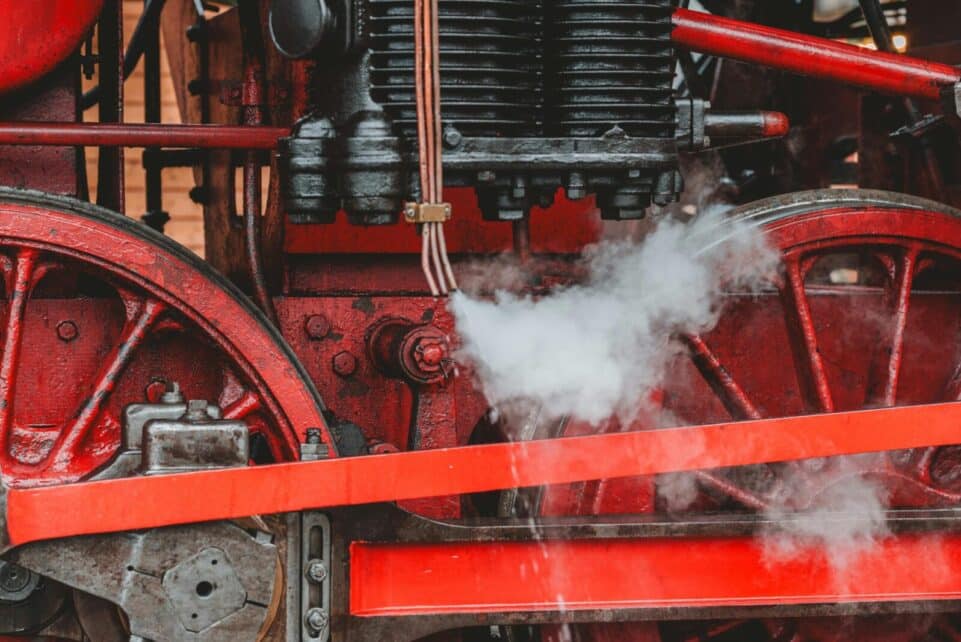 Detailed view of a red vintage steam locomotive engine showcasing gears and steam.