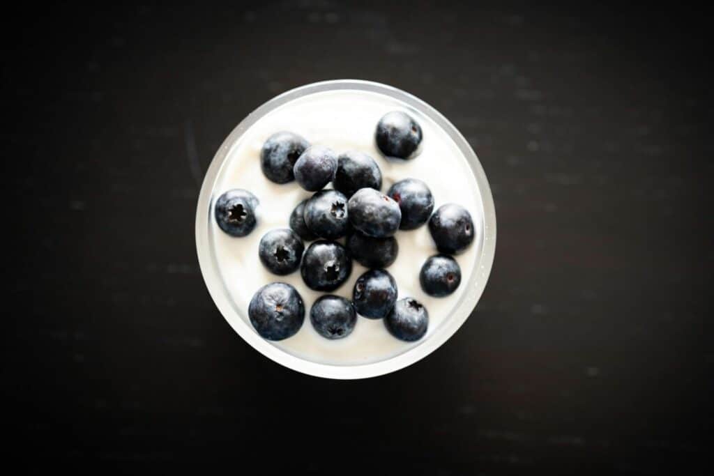 Top view of creamy yogurt with fresh blueberries in a glass bowl on a dark background.