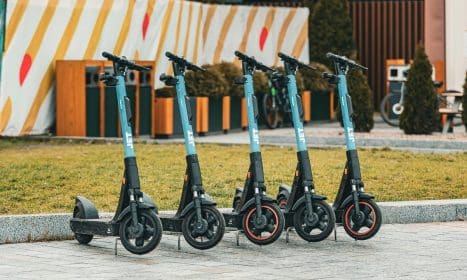 Group of five electric scooters neatly lined up outdoors, ready for rental use.