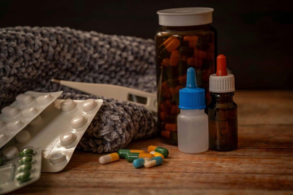 Collection of flu remedies including pills, thermometer, and scarf for winter cold relief.