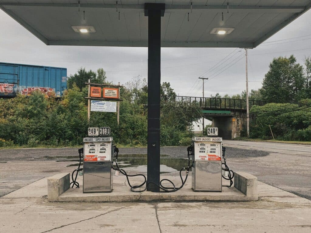 An outdoor scene of an abandoned gas station with dual pumps and vivid greenery in the background.