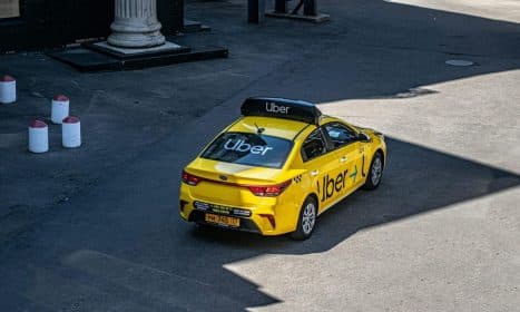 A yellow Uber taxi driving on a city street, shown from above.