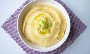 Top-down view of creamy mashed potatoes garnished with scallion in a white bowl.