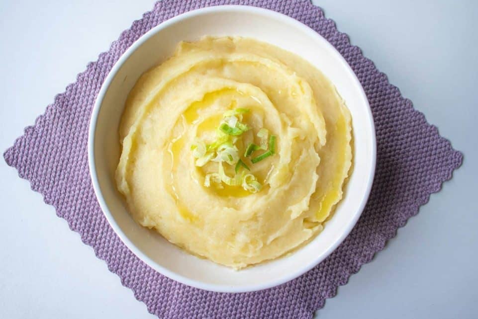 Top-down view of creamy mashed potatoes garnished with scallion in a white bowl.