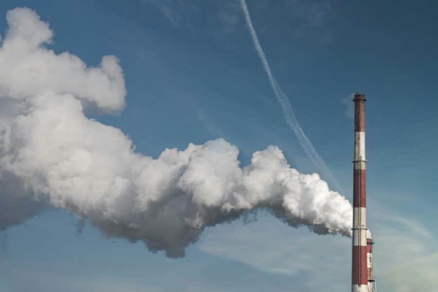 Smoke stack with billowing clouds against a blue sky, highlighting pollution.