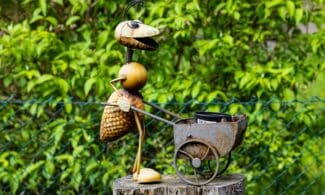 Charming metal ant sculpture with wheelbarrow in lush summer garden setting.