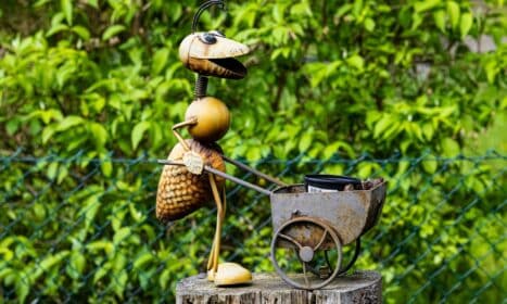Charming metal ant sculpture with wheelbarrow in lush summer garden setting.