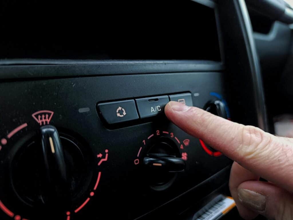 Close-up of a person adjusting a car's air conditioning system inside a vehicle cabin.
