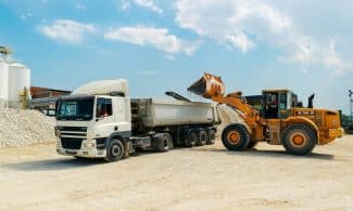 Excavator loading materials into a heavy-duty truck at a sunny construction site.