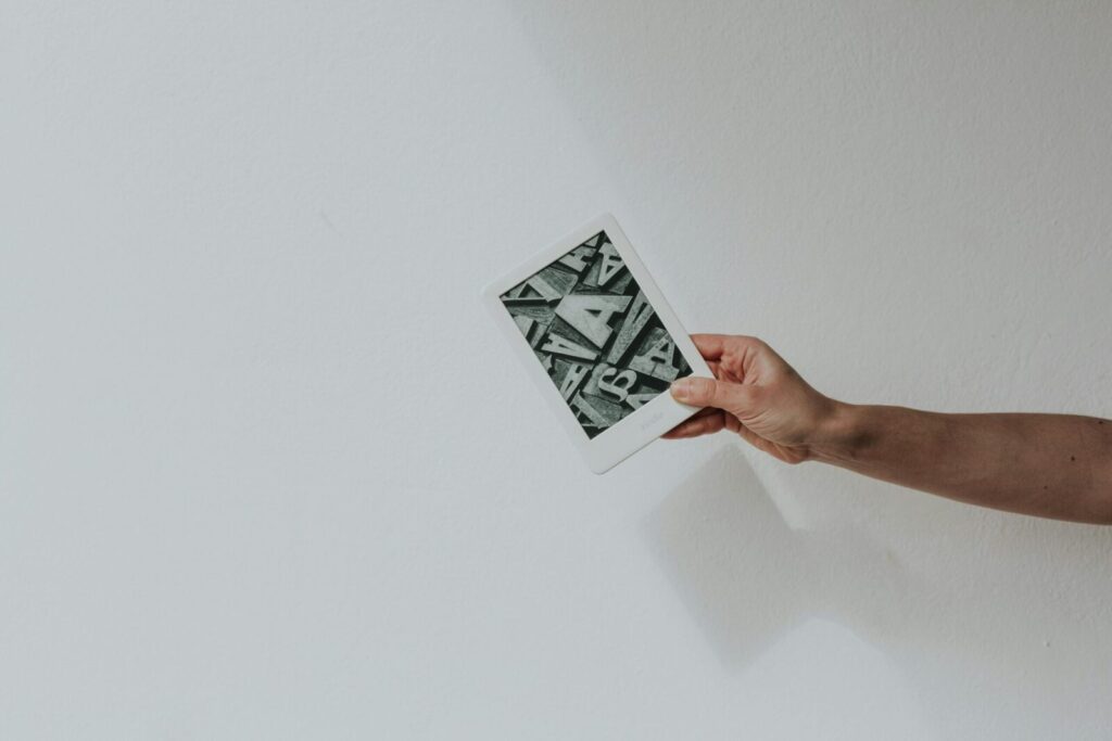 A minimalist photo of a hand holding a modern e-reader against a white background.