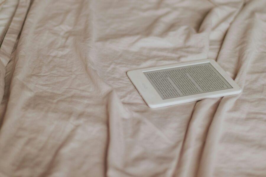 A minimalist e-reader resting on a beige crumpled bedspread, evoking a cozy reading environment.