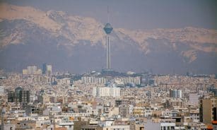 Aerial view of Tehran featuring Milad Tower against the Alborz Mountains.