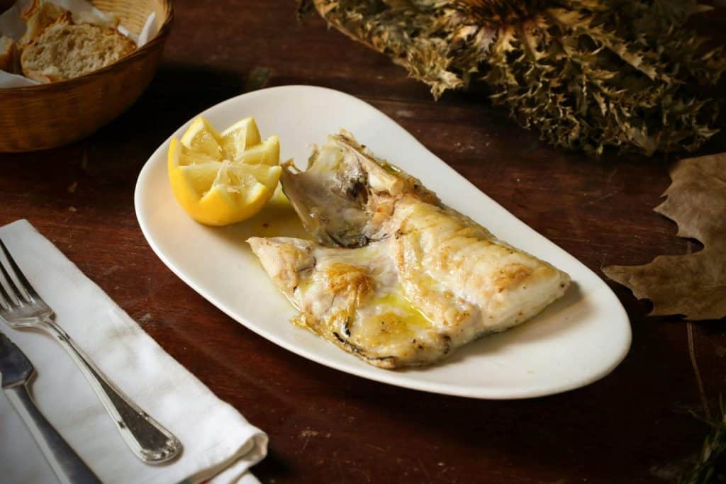 A plate of grilled fish served with lemon, bread, and a rustic autumn setting.