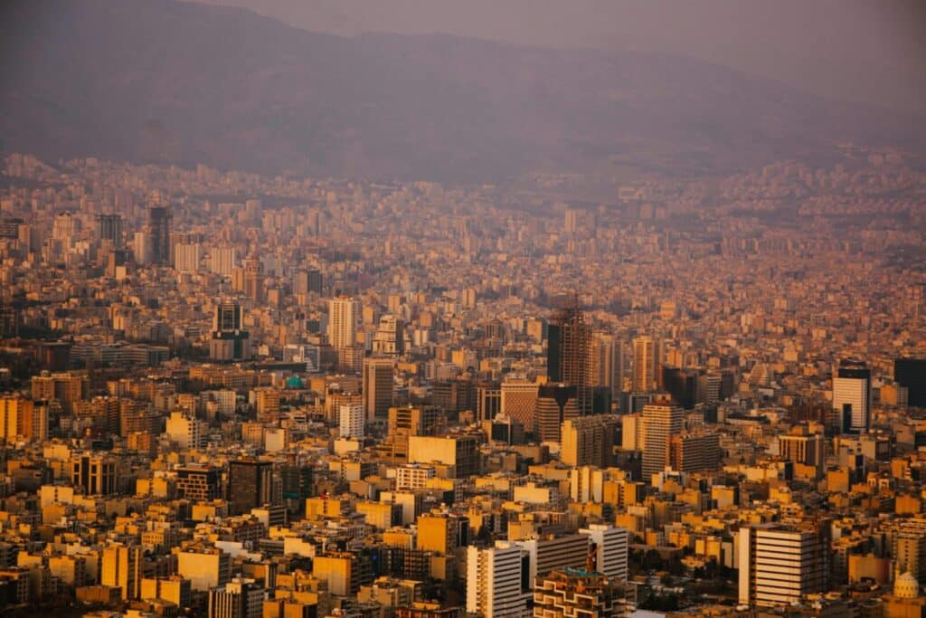 A sprawling view of Tehran's urban landscape with mountains in the background at sunset.