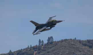 F-16 fighter jet flying over hills in Kernville, California, under a clear blue sky.