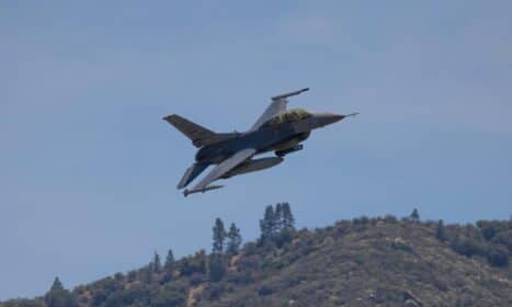 F-16 fighter jet flying over hills in Kernville, California, under a clear blue sky.