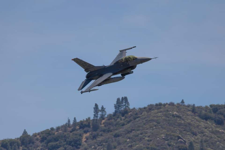 F-16 fighter jet flying over hills in Kernville, California, under a clear blue sky.