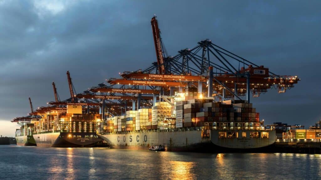 Illuminated container ships and cranes at Hamburg port during nighttime, showcasing global shipping.