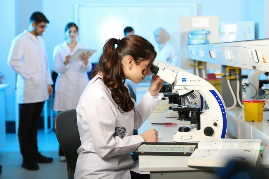 Young female scientist examining samples under a microscope in a modern laboratory setting.