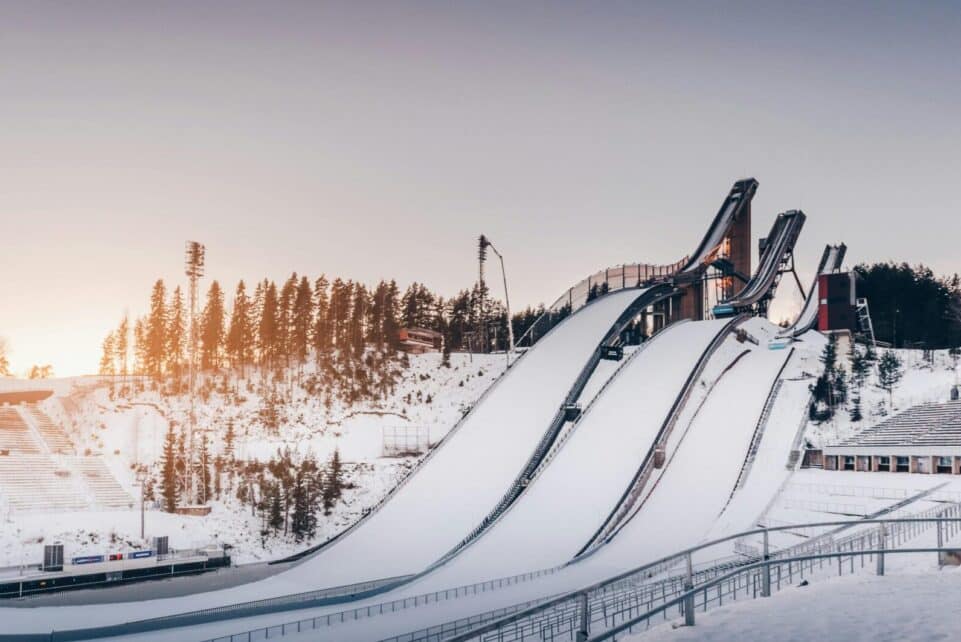 Snow-covered ski jumps in Lahti during winter golden hour with a serene and frosty landscape.