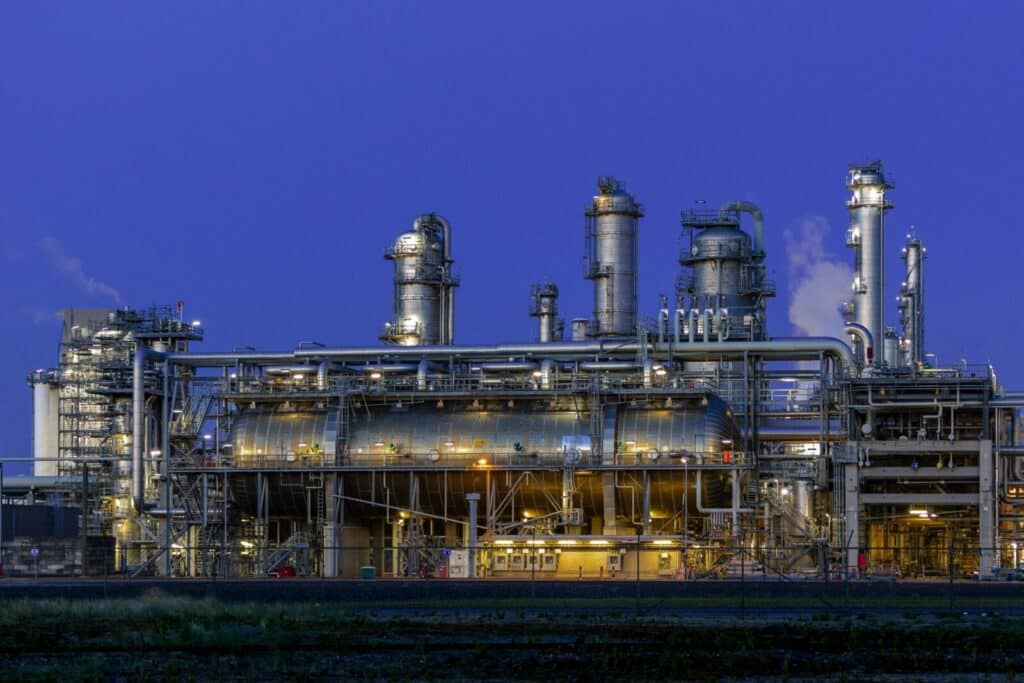 A striking view of an industrial facility in Zuid-Holland, illuminated at dusk against a clear blue sky.