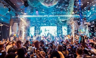 Vibrant nightclub scene in Mantua, Italy, featuring a lively crowd, confetti, and colorful lights.