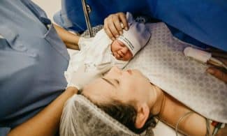 A mother cradling her newborn immediately after childbirth in a hospital setting.