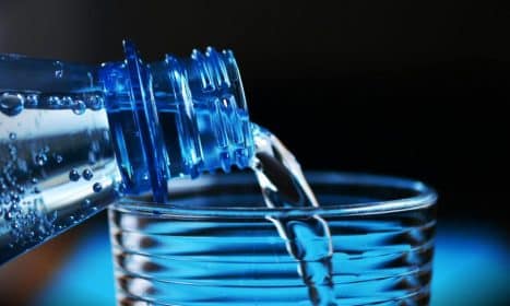Close-up of sparkling water being poured from a bottle into a glass with bubbles visible.