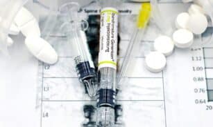 Close-up of syringes and pills on a bone density exam sheet, depicting osteoporosis treatment.