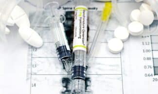 Close-up of syringes and pills on a bone density exam sheet, depicting osteoporosis treatment.