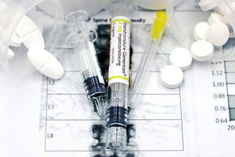 Close-up of syringes and pills on a bone density exam sheet, depicting osteoporosis treatment.