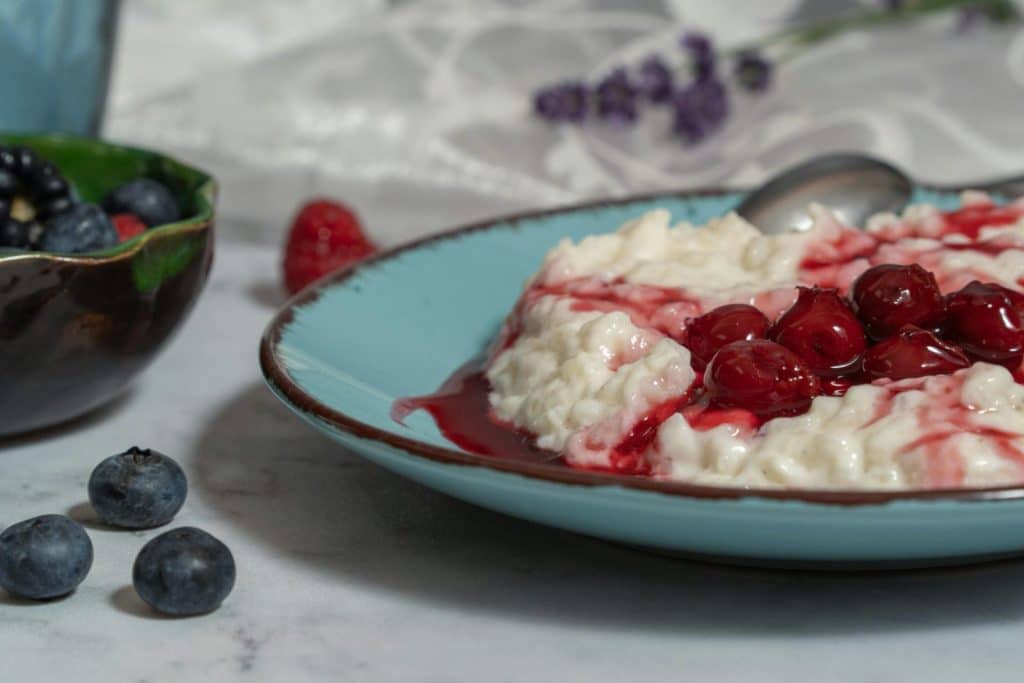 Creamy rice pudding topped with cherries and surrounded by fresh berries in a cozy setting.