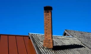 A solitary brick chimney rises from a tiled roof under a vibrant blue sky, showcasing minimal architecture.