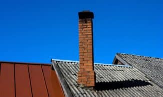 A solitary brick chimney rises from a tiled roof under a vibrant blue sky, showcasing minimal architecture.